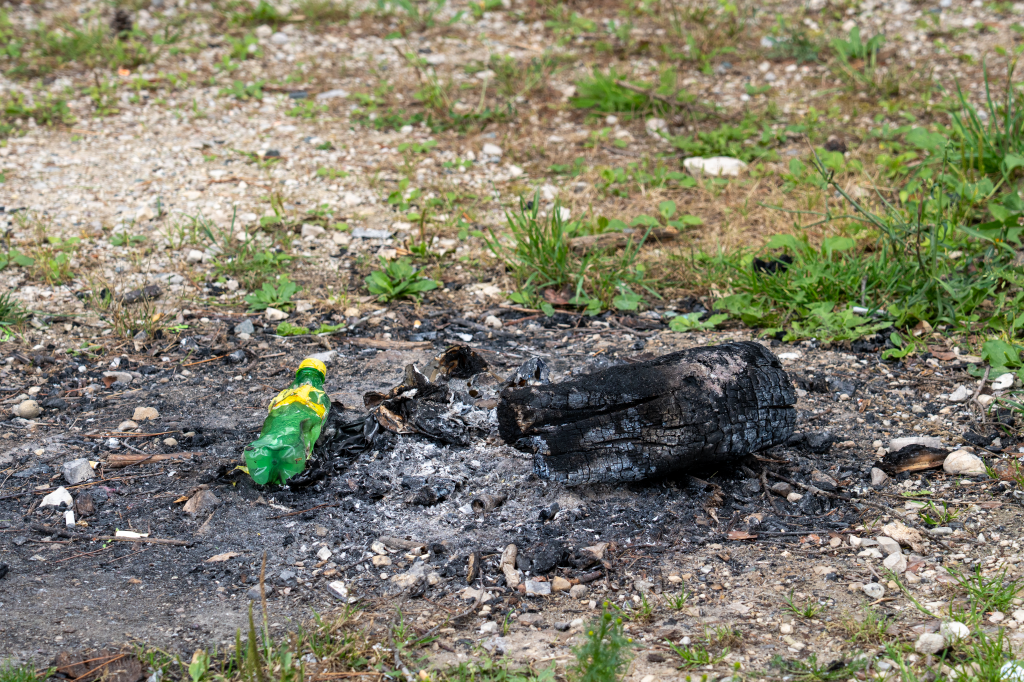 Melted plastic bottle, next to burned log that is on the ground and not in a fire pit.