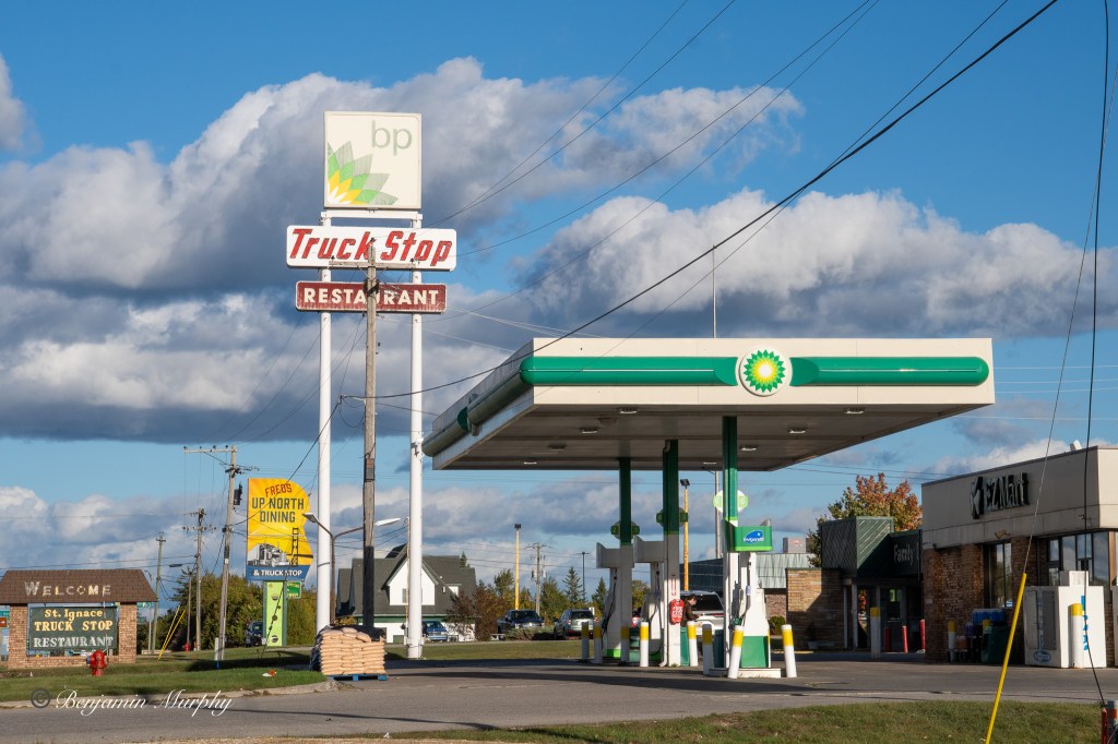 Photo of a gas station in Saint Ignace, showing the pumps, station sign, and station name.