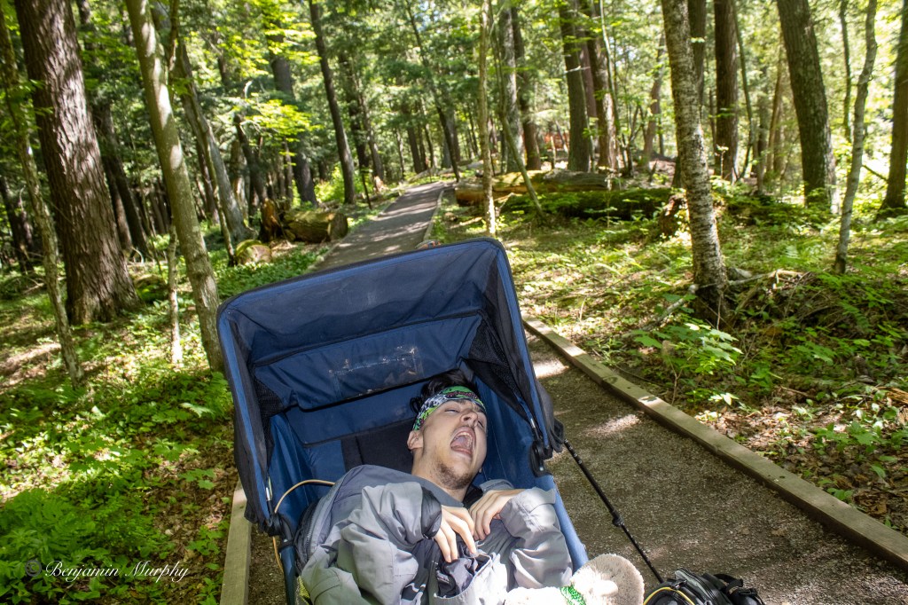 Tristan in a jogging wheelchair smiling during an early morning hike.